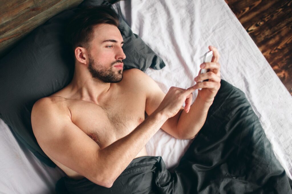Homem sem camisa na cama vendo pornografia. 